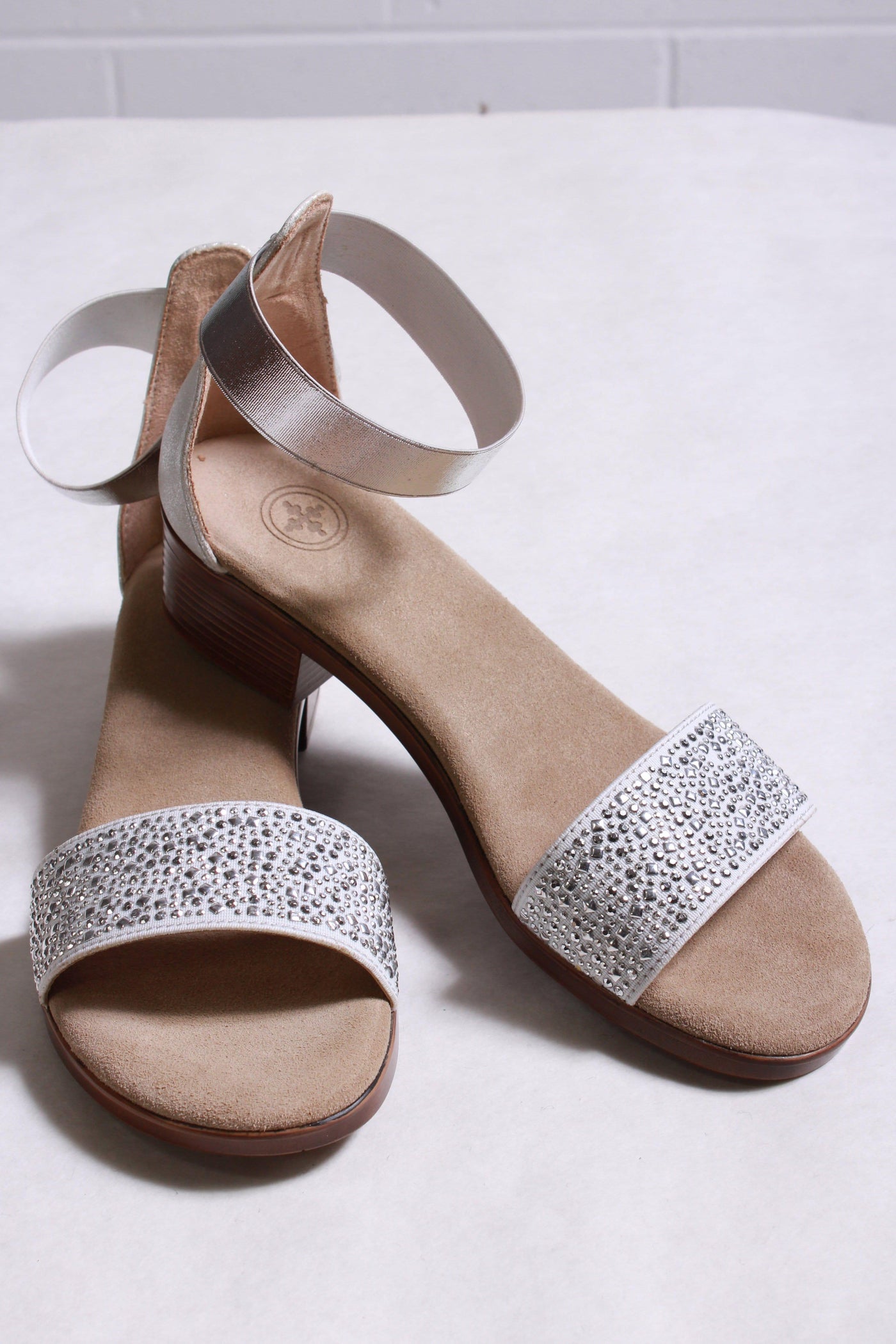 side of silver sandal has a sparkled toe strap and a 1" heel  with an elastic band ankle strap