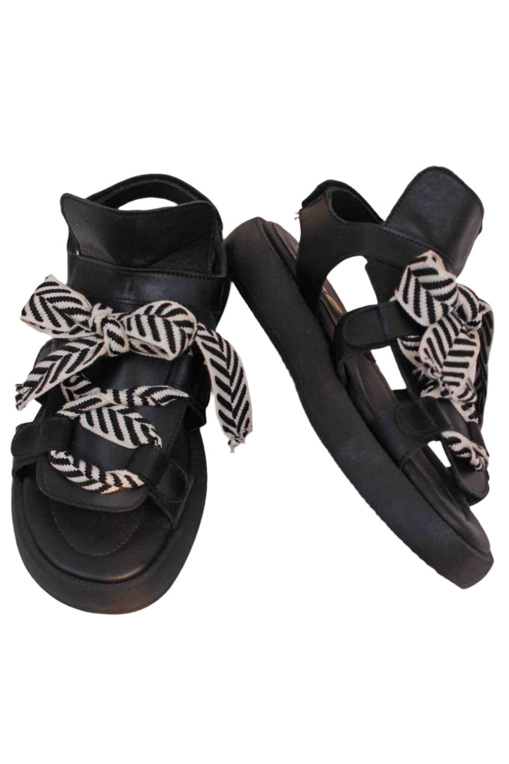 Black Leather Bowlace Sandals by All Black with one shoe angled on it's side