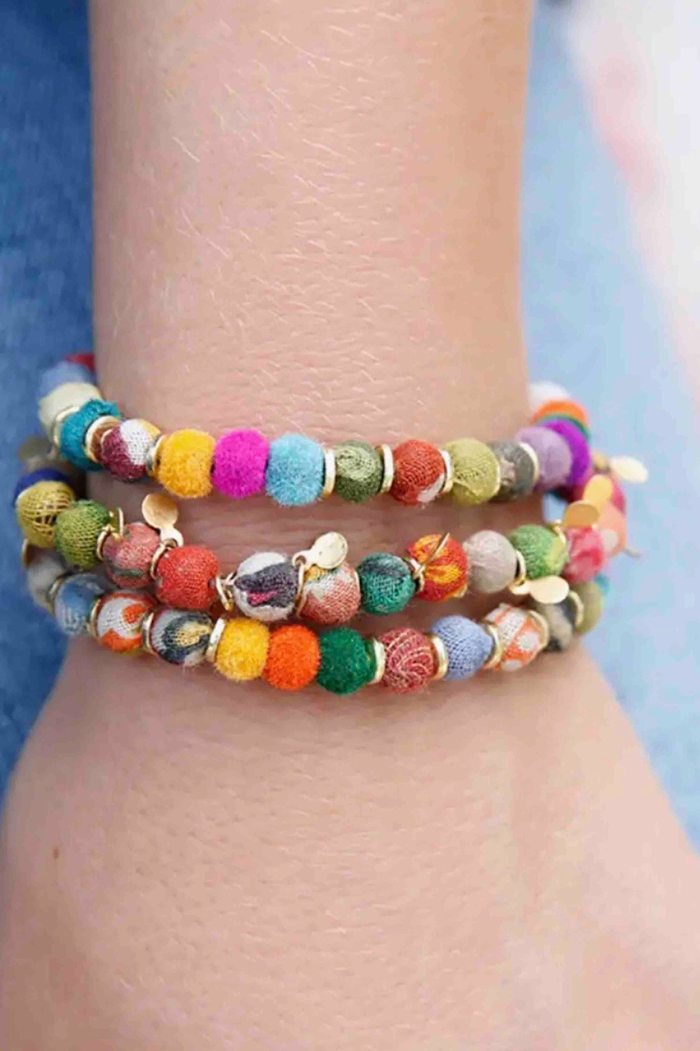 model wearing 2 Multicolored Kantha Pom Pom Bracelets by World Finds with a different one in the middle