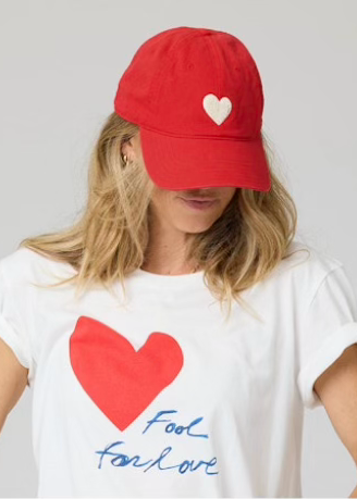 model wearing the Cherry Red KR Imperfect Hat by Kerri Rosenthal with a White Chenille Heart and the Suke Fool for Love Tee