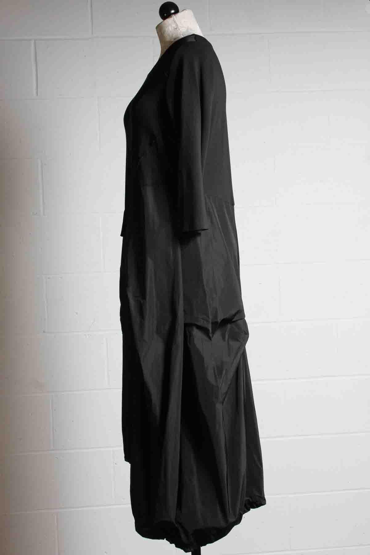 side view of black long sleeve dress by Reina Lee with an asymmetrical gathered bottom in contrasting fabrics