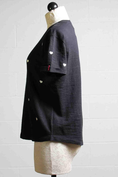 side view of Black Show Me Love Top By Lisa Todd with White tiny hearts all over the front and sleeves and a tiny purple down on the bottom left